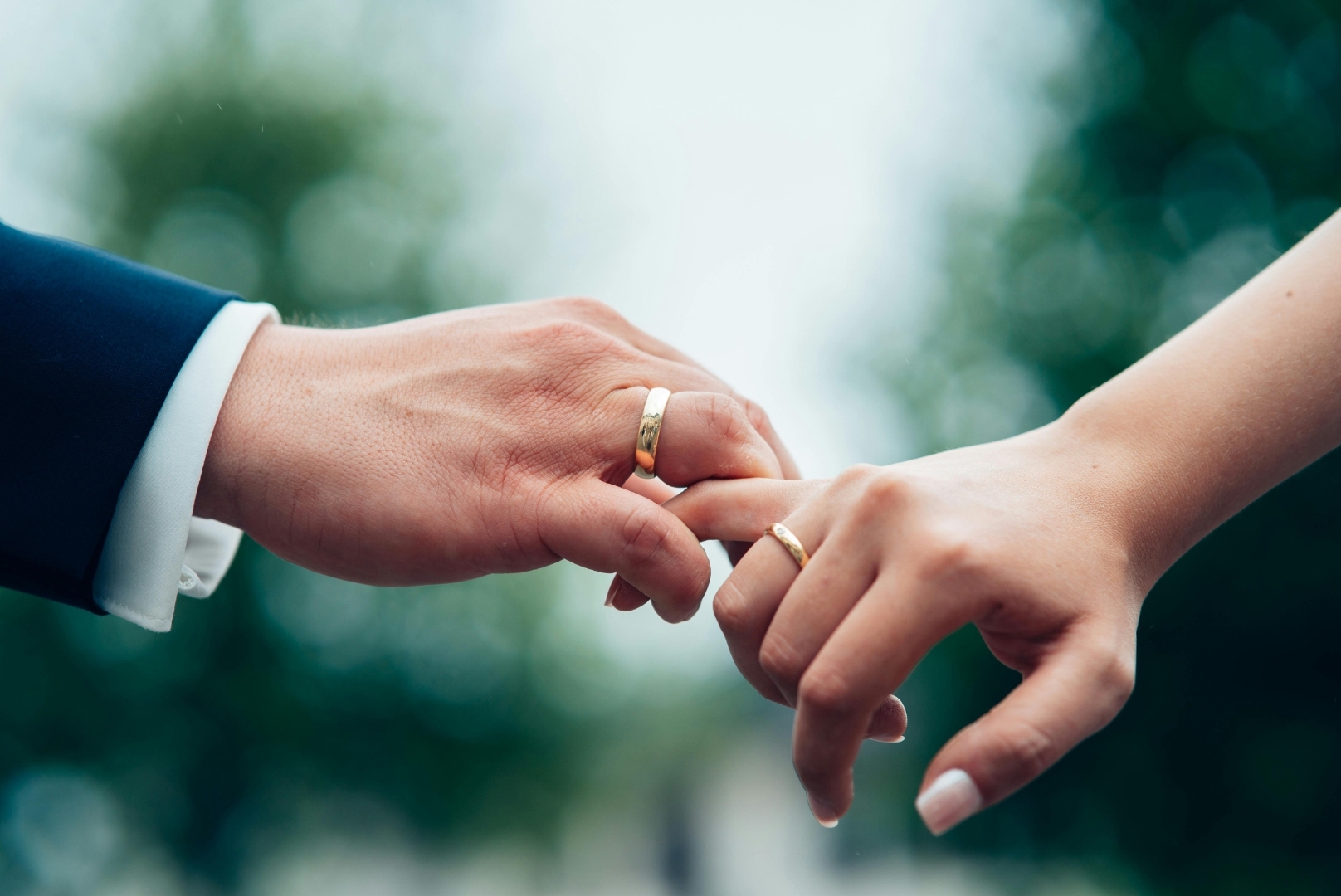 Close-up of two hands wearing wedding rings gently touching each other.